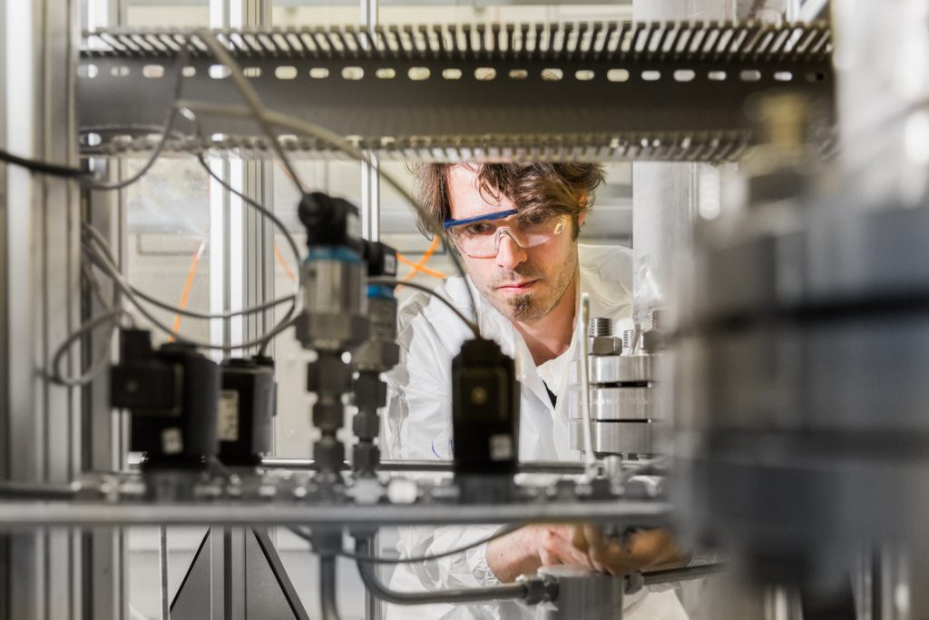 Blick durch einen Teststand, ein Wissenschaftler schaut von der anderen Seite hinein