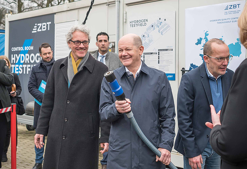 Bundeskanzler Olaf Scholz hält Tankadapter einer Wasserstofftankstelle in der Hand
