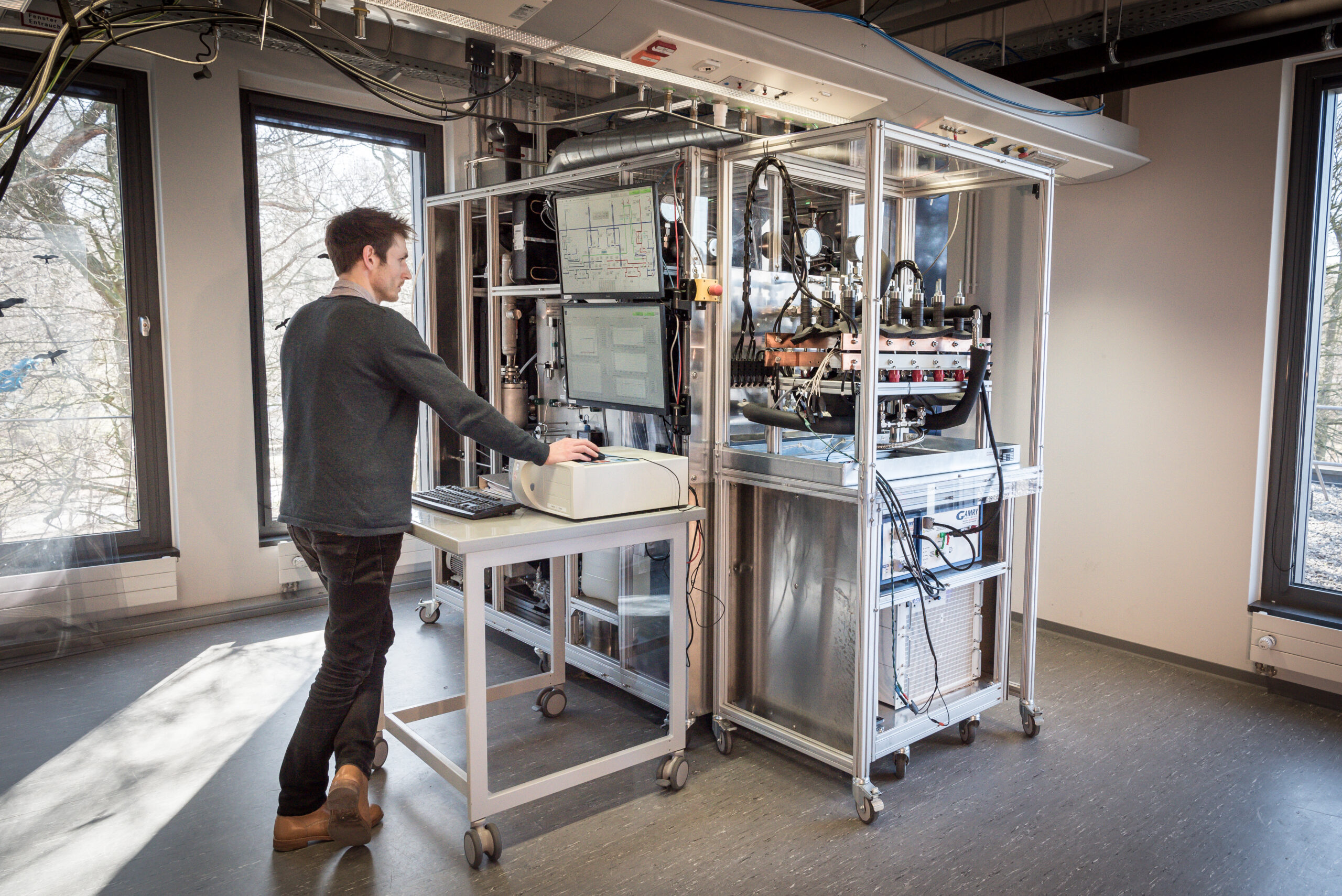 Mann steht an Elektrolyse-Teststand, den er über einen Computer steuert.