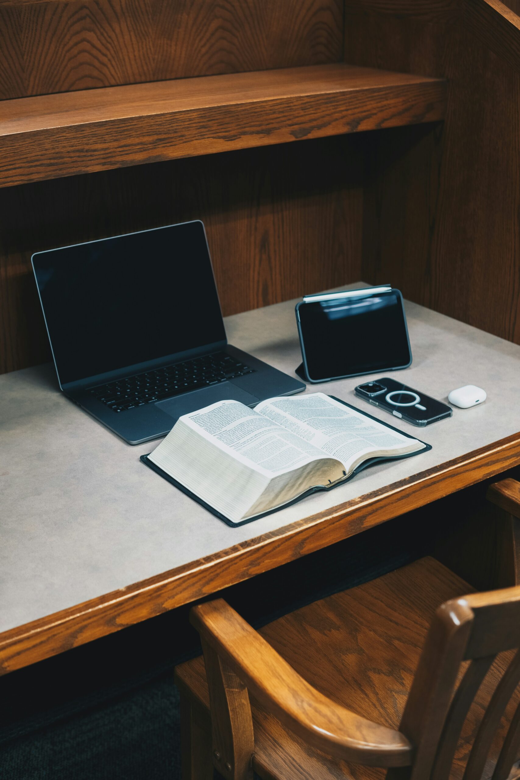Schreibtisch mit einem geöffneten Laptop, einem aufgeschlagenen Buch und einerm Mobiltelefon