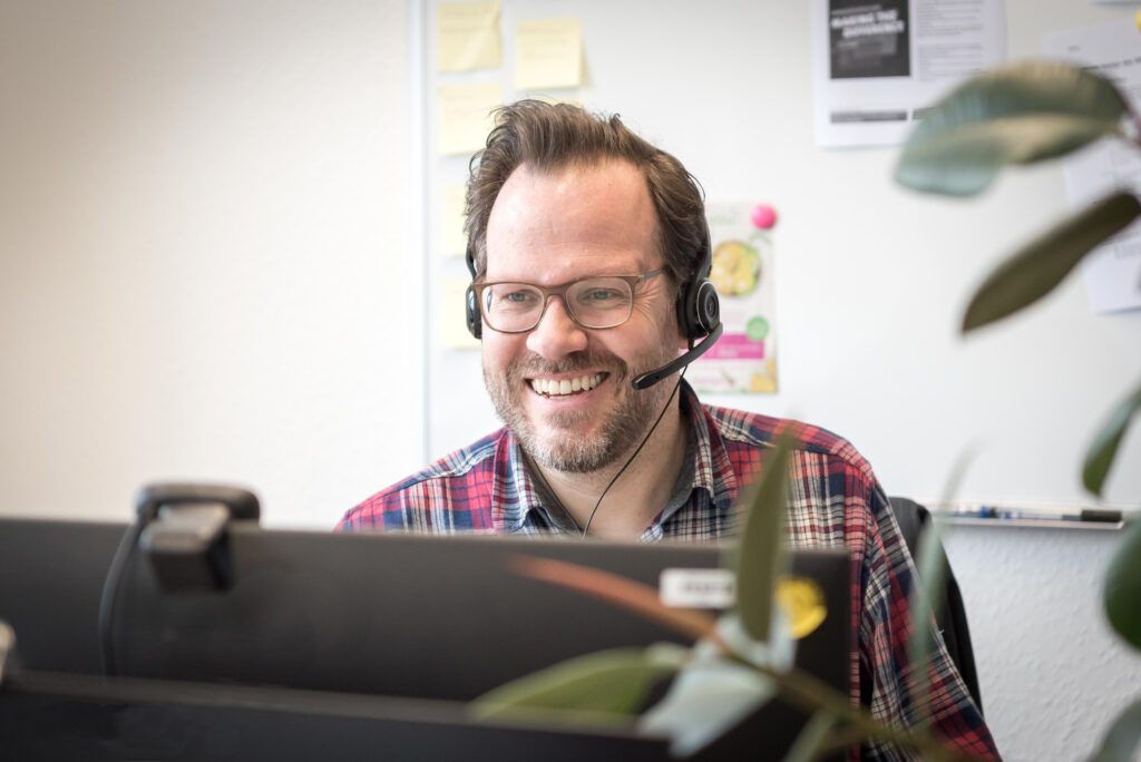 Bürosituation mit Mann mit Headset hinter einem Monitor